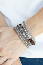 Load image into Gallery viewer, Mismatched sections of glassy and opaque gray beads join silver discs, brown wooden beads, and gray disc-like beads along a coiled wire, creating an earthy infinity wrap bracelet around the wrist.
