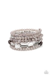 Mismatched sections of glassy and opaque gray beads join silver discs, brown wooden beads, and gray disc-like beads along a coiled wire, creating an earthy infinity wrap bracelet around the wrist.