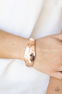 The front of a thick rose gold bangle-like bracelet is stamped in a leafy floral pattern, creating a whimsy centerpiece around the wrist. Features a hinged closure.