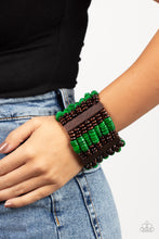 Load image into Gallery viewer, Held together by rectangular wooden frames, rows of brown wooden and distressed Leprechaun discs are threaded along stretchy bands around the wrist for a seasonal pop of color around the wrist.
