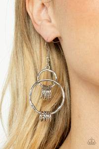 An antiqued collection of dainty silver rings swings from the bottoms of hammered silver hoops that interconnect into an edgy lure. Earring attaches to a standard fishhook fitting.