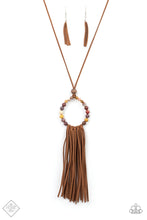 Load image into Gallery viewer, A collection of earthy multicolored stone beads are threaded around a wire hoop that is fastened at the end of a lengthened brown suede cord. The earthy stones make way for a foxy fringe of brown suede that sways from the bottom of the hoop, resulting in a rustic down-to-earth vibe. Features an adjustable clasp closure.  Sold as one individual necklace. Includes one pair of matching earrings.
