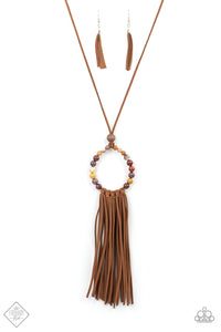 A collection of earthy multicolored stone beads are threaded around a wire hoop that is fastened at the end of a lengthened brown suede cord. The earthy stones make way for a foxy fringe of brown suede that sways from the bottom of the hoop, resulting in a rustic down-to-earth vibe. Features an adjustable clasp closure.  Sold as one individual necklace. Includes one pair of matching earrings.