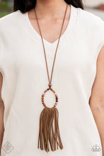 Load image into Gallery viewer, A collection of earthy multicolored stone beads are threaded around a wire hoop that is fastened at the end of a lengthened brown suede cord. The earthy stones make way for a foxy fringe of brown suede that sways from the bottom of the hoop, resulting in a rustic down-to-earth vibe. Features an adjustable clasp closure.  Sold as one individual necklace. Includes one pair of matching earrings.
