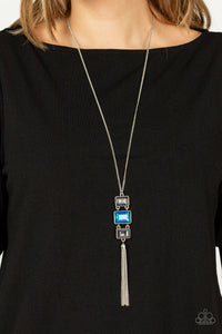 A sparkly collection of mismatched smoky, blue, and hematite rectangular gems stack at the bottom of a lengthened silver chain, creating a glamorous pendant. A dainty silver chain tassel swings from the bottom, adding glamorous movement to the modern display. Features an adjustable clasp closure.