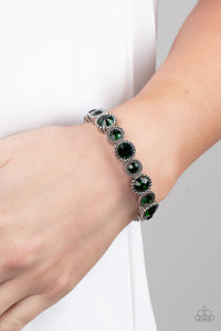 Sparkling green gems are encased in studded silver frames. Varying in size, smaller gems alternate with larger gems along stretchy bands around the wrist for a dramatic look. 