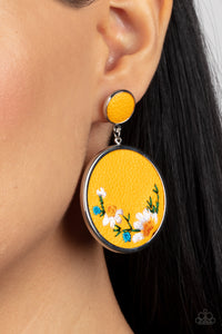 A small yellow leather disc, encased in a simple silver frame, anchors a larger yellow circle that is adorned with fanciful embroidered flowers creating a whimsical lure. Earring attaches to a standard post fitting.