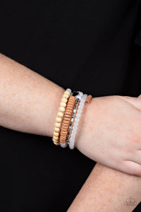 Mismatched sections of glassy and opaque white beads join silver discs, brown wooden beads, and brown disc-like beads along a coiled wire, creating an earthy infinity wrap bracelet around the wrist. 