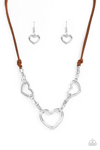 Strands of brown suede knot around sections of chunky silver chains that have been adorned in oversized silver heart frames, resulting in a flirtatious display below the collar. Features an adjustable clasp closure.