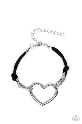Strands of black suede knot around sections of chunky silver chains that have been adorned in an oversized silver heart frame, resulting in a flirtatious display around the wrist. Features an adjustable clasp closure.