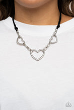 Load image into Gallery viewer, Strands of black suede knot around sections of chunky silver chains that have been adorned in oversized silver heart frames, resulting in a flirtatious display below the collar. Features an adjustable clasp closure.
