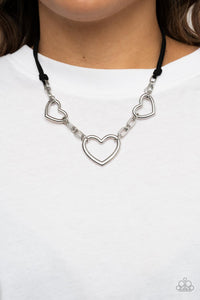 Strands of black suede knot around sections of chunky silver chains that have been adorned in oversized silver heart frames, resulting in a flirtatious display below the collar. Features an adjustable clasp closure.