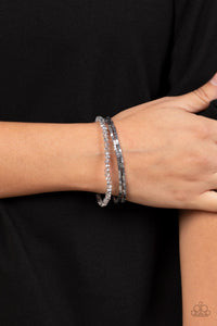 Two rows of dainty silver cube beads and one row of smoky crystal-like beads are threaded along stretchy bands around the wrist, creating stellar layers. 