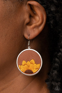 A golden yellow and brown threaded sunflower is stitched into the bottom of a brown leather frame that is encased in a sleek silver frame, resulting in a whimsical floral fashion. Earring attaches to a standard fishhook fitting.