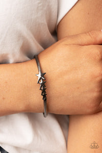 Glistening gunmetal stars graduate in size across the center of a textured gunmetal bangle, creating a stackable stellar centerpiece around the wrist. 