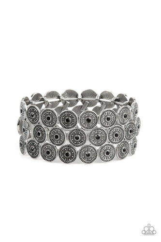 Dotted with dainty black rhinestone centers, studded silver discs haphazardly stack into trios that have been threaded along stretchy bands around the wrist for a whimsical finish.