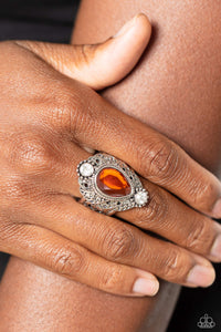 Glassy white rhinestones flank a mystically oversized burnt orange teardrop atop folds of studded and filigree filled silver ruffles, culminating into an enchanting centerpiece atop a decorative silver band. Features a stretchy band for a flexible fit.