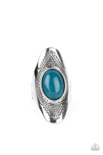 An oversized, glassy, blue bead is pressed into the center of a dramatically elongated silver frame. Triangular patterns are etched into the frame as it folds around the finger, resulting in an ethereal pop of color atop the finger. Features a stretchy band for a flexible fit.