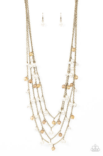 Row after row of bubbly white pearls and brassy crystal-like beads swing from layered brass chains across the chest, creating a noise-making display. Features an adjustable clasp closure. 