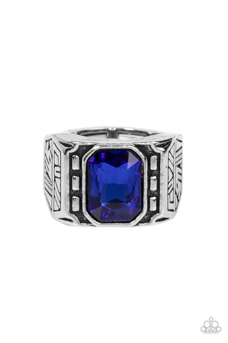 A majestic emerald cut blue rhinestone is pressed into the center of a rectangular studded silver frame flanked by geometric texture, creating an edgy centerpiece atop the finger. Features a stretchy band for a flexible fit.