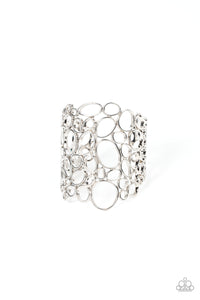 Varying in shape and size, asymmetrical silver circular frames delicately connect into an effervescently abstract cuff around the wrist.