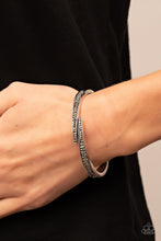 Load image into Gallery viewer, Encrusted in stacked sections of antiqued silver studs and smoky hematite rhinestones, two silver bars delicately overlap at the center of the wrist, resulting in an edgy cuff-like bangle. Features a hinged closure.

