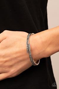 Encrusted in stacked sections of antiqued silver studs and smoky hematite rhinestones, two silver bars delicately overlap at the center of the wrist, resulting in an edgy cuff-like bangle. Features a hinged closure.