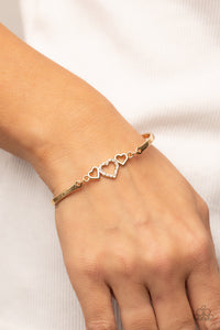 Two shiny gold hearts flank a white rhinestone dotted heart at the center of two curved gold bars, linking into a flirtatious centerpiece around the wrist. Features an adjustable clasp closure. 