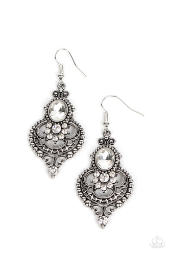 A white rhinestone floral accent flares out from the bottom of an oversized oval gem atop a studded backdrop of silver filigree, resulting in a regal lure. Earring attaches to a standard fishhook fitting. 