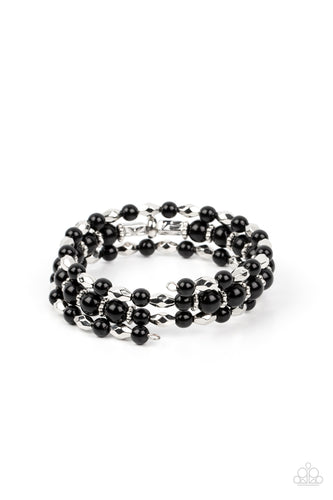 A mismatched collection of faceted silver beads, studded silver rings, and polished black beads are threaded along a wire that coils around the wrist, creating a colorful infinity wrap style bracelet. 