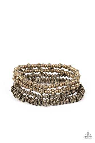 An antiqued assortment of studded, round, and decorative brass beads are threaded along stretchy bands around the wrist, creating rustic layers. 