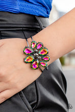 Load image into Gallery viewer, A dazzling collection of oil spill teardrop gems dramatically fan out around three round pieces of hematite, creating an explosion of sparkle. The exaggerated gems circle into a floral centerpiece that sits atop a pair of skinny gunmetal bars that wrap around the wrist in an airy finish. Features a hinged closure.
