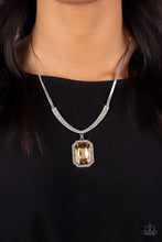 Load image into Gallery viewer, An oversized, topaz, emerald-cut gem is bordered by tiny white rhinestones and dizzying studded texture, creating a smoldering pendant that swings from the bottom of a curved bar. White rhinestones lay side-by-side along the curved bar of silver, graduating in size as they climb the neckline and connect to a flat silver snake chain in a sleek finish. Features an adjustable clasp closure.
