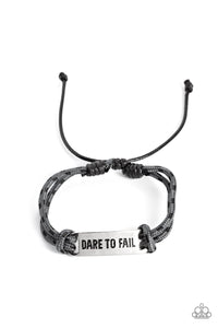Gray paracord rope, sporadically dotted with black spots, encircles a square silver pendant. Featured on the pendant, the phrase "Dare to Fail" is stamped in bold lettering for an urban, inspirational statement around the wrist. Features an adjustable sliding knot closure. 