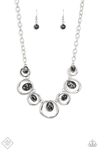 Marbled black stones are encased in classic silver frames and attached to the inside edges of warped silver hoops. The haphazard placement of the stones and the irregular shape of the silver rings add a handcrafted touch to the design, as the asymmetrical frames fall along the collar at the end of a thick silver chain. Features an adjustable clasp closure. As the stone elements in this piece are natural, some color variation is normal.