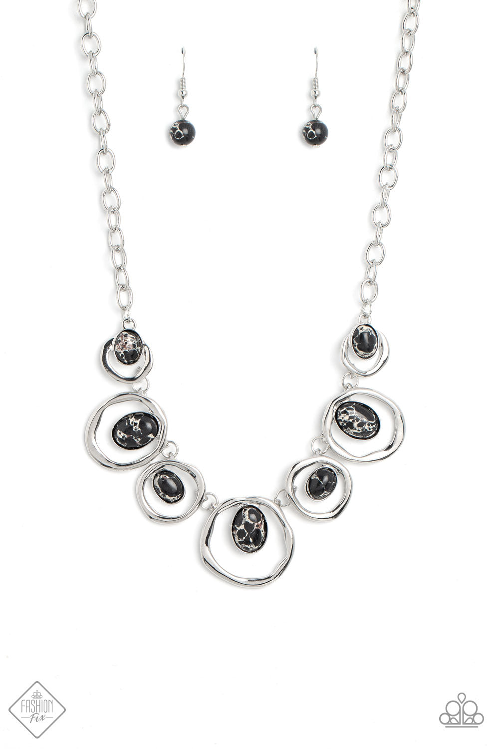 Marbled black stones are encased in classic silver frames and attached to the inside edges of warped silver hoops. The haphazard placement of the stones and the irregular shape of the silver rings add a handcrafted touch to the design, as the asymmetrical frames fall along the collar at the end of a thick silver chain. Features an adjustable clasp closure. As the stone elements in this piece are natural, some color variation is normal.