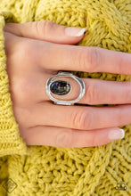 Load image into Gallery viewer, A marbled black stone is wrapped in a thin border of silver and attached to the inside edge of a warped oval frame. The open frame allows the skin to peek through, creating a unique statement piece atop the finger. Features a stretchy band for a flexible fit. As the stone elements in this piece are natural, some color variation is normal.  Sold as one individual ring.
