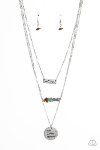 A silver rectangular plate, stamped with a mountain outline swings from the uppermost chain above a row of chiseled tiger's eye, jade, lapis, and amethyst stones. An oversized shimmery silver disc stamped with the phrase 