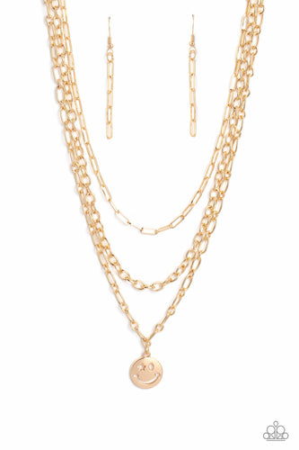 A trio of gold paperclip, classic, and oval link chains coalesces down the neckline for a monochromatic masterpiece. Strung on the lowermost oval link chain, a gold smiley face pendant, with a star mimicking a wink for one of its eyes, stands out and reflects light in every direction for a statement finish. Features an adjustable clasp closure.