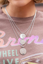 Load image into Gallery viewer, Three silver discs trickle from the bottom of three silver snake chains, creating shimmery monochromatic layers down the chest. An intricate floral design is stamped onto each disc, adding a whimsical touch to the charming design. Features an adjustable clasp closure.  Sold as one individual necklace. Includes one pair of matching earrings.
