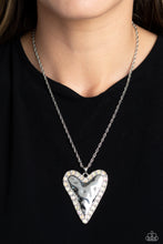 Load image into Gallery viewer, Hammered in antiqued texture, an oversized, abstract silver heart swings from the bottom of a silver chain for a whimsical look. Silver studs and glittery iridescent gems border the hammered texture for a touch of bling. Features an adjustable clasp closure. Due to its prismatic palette, color may vary. 
