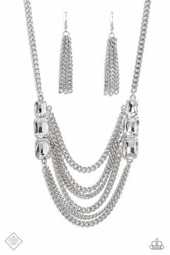 Layers of thick, silver curb chain drape across the chest, creating a fierce, industrial statement piece. Three blinding white, emerald-cut gems that gradually increase in size, are affixed to each side of the swooping chains, adding dramatic sparkle to the collision of grit and glitz. Features an adjustable clasp closure.