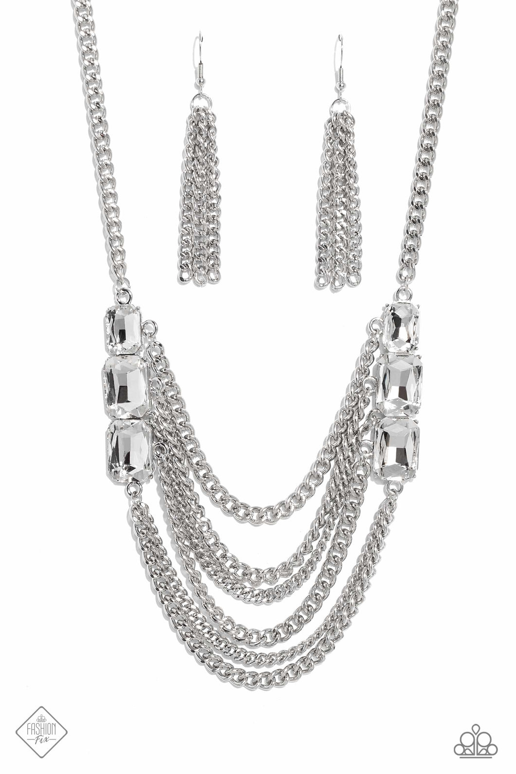 Layers of thick, silver curb chain drape across the chest, creating a fierce, industrial statement piece. Three blinding white, emerald-cut gems that gradually increase in size, are affixed to each side of the swooping chains, adding dramatic sparkle to the collision of grit and glitz. Features an adjustable clasp closure.
