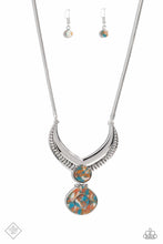 Load image into Gallery viewer, A thick, silver, v-shaped frame, with airy, vented cutouts, sits boldly at the end of a silver snake chain. A widened teardrop-shaped stone, marbled with swirls of blue, white, and brown, sits at the center of the dramatic frame, adding a pop of color to the regal design. A second teardrop-shaped stone — with a third, smaller stone nestled within a silver border at its center — swings from the polished stone above, adding eye-catching movement and intriguing detail. 
