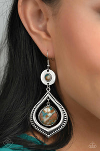 A brown stone marbled with blue and white is pressed into a thick circular silver frame. Dangling from the circular frame, an oversized silver spade-like frame etched in rural textures, features a larger brown stone marbled with blue and white, swinging from the top of the frame for an earthy lure. Earring attaches to a standard fishhook fitting. As the stone elements in this piece are natural, some color variation is normal.