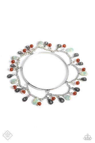 Featuring mismatched finishes, marbled blue stone teardrops, studded silver teardrops, and glassy brown beading swings from a shimmery silver chain, creating an earthy fringe. The chain is attached to a skinny silver bangle, looping into a scalloped pattern to allow whimsical movement around the wrist. 