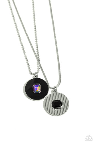 Two various dainty silver chains, one a snake and the other a ball, delicately layer below the collar. A black-painted pendant with a dainty emerald-cut UV gem center sparkles at the bottom of the uppermost ball chain, while a textured silver pendant with a horizontally placed emerald-cut black gem swings from the bottom of the snake chain display for a mystical finish. Features an adjustable clasp closure.
