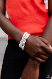 Strung along elastic stretchy bands, three strands of high-sheen classic white pearls wrap around the wrist. Featured atop the pearly collection, a loopy silver bow, filled with glistening white rhinestones is attached to the center of the wrist for a dramatically dazzling finish.
