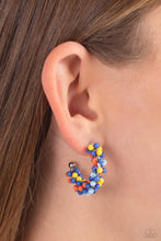 Load image into Gallery viewer, A colorful collection of royal blue, yellow, light blue, and orange seed beads are wrapped along the outside curve of a shiny, silver hoop by shimmery silver wire for a handcrafted, carefree finish. A shiny silver ball is affixed to the end of the hoop, reminiscent of a barbell fitting. Earring attaches to a standard post fitting. Hoop measures approximately 1&quot; in diameter. 
