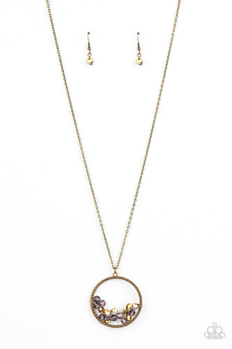A cluster of metallic flecked aurum and iridescent crystal-like beads are threaded along dainty brass wire along the bottom of a textured brass hoop, creating a stellar pendant at the bottom of a lengthened brass chain. Features an adjustable clasp closure.  Sold as one individual necklace. Includes one pair of matching earrings.